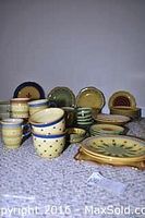 Overview of various plates, bowls, mugs, and serving pieces with yellow, cream, green, and blue decoration set out on table.
