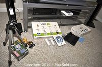 Photo showing tripod, Fujifilm camera box, camera, 35mm film, Wii Fit and Wii Sports game boxes, white Wii controllers and balance board on carpet floor below a glass TV stand.