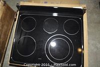 Top down view of black glass-ceramic GE stove top showing all five burners in original box.