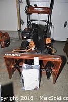 Front view of Craftsman snowblower with manual in plastic sleeve strapped to auger housing and orange extension cord wrapped around chute