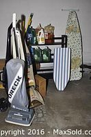 Full view of the cleaning assortment including ironing boards, shelf with cleaning liquids, and vacuum cleaner with cords on concrete floor