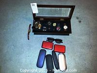 Overview of men's watch collection with wooden case, multiple watches and accessories including eyeglass cases and sunglasses.