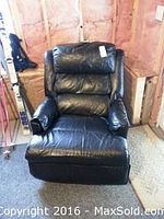 Front view of the black leather recliner chair showing padded backrest, cushioned armrests and seat with wear marks and paint spots.