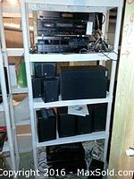 White shelving unit with stacked electronics on top shelf and various black speakers on lower shelves