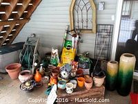 Wide view of gardening supplies including multiple pots, soil bags, garden hoses, small garden tools, and decorative items arranged on porch floor under stairs.