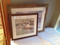 Two framed prints leaning together on a flat surface, showing both pieces and their wooden frames.