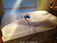 Single white electric adjustable bed on carpeted floor next to window with blinds.