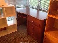 L-shaped wood desk with 3 drawers and keyboard pull-out, near window and other furniture.