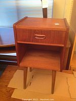 Nightstand front view with drawer closed, showing teak veneer finish and tapered legs.