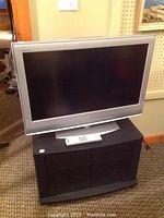 Front view of Sony Bravia TV sitting on black TV stand with remote placed on top