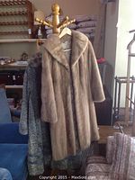 Two fur coats hanging on a wooden coat rack, one light brown mink, the other grey lambs fur.