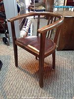 Full view of barrel chair showing curved wooden backrest and leather seat on carpeted floor.