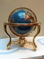 Front view of decorative world globe with blue marble oceans and mixed colored marble inlaid continents seated on brass tripod stand.