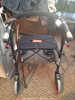 Full view of the folding walker showing frame, padded seat, wheels, and cane leaning against it.