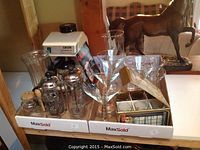 Photo shows Gaggia espresso machine with manual, assorted glassware including coffee presses, stemware, and other glass containers arranged on two boxes.