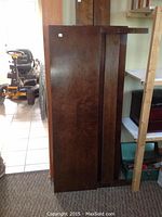 Side view of a large rectangular wooden panel with walnut veneer finish, part of bed components leaning against a wall.