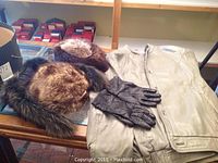 Grey ladies leather jacket, two fur hats, dark brown fur collar and black leather gloves on table.
