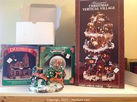 Photo of boxes showing Illuminated Christmas Vertical Village, Dickensville Collectible house, and musical snow globe.