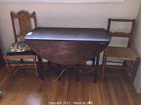 Wood gate leg drop-leaf table and two wood chairs positioned on hardwood floor near a wall.