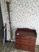 Photo showing full view of the metal coat rack, small wooden dresser, and two umbrellas leaning against the wall.