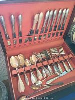 View inside the storage box showing rows of knives, forks, spoons, and serving utensils arranged neatly.