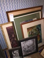 Overall group of framed art and relief pieces leaning against a wall, showing a variety of frame styles and sizes.