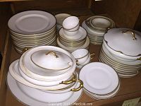 Full assortment showing stacked plates, cups with saucers, covered tureens and casseroles with gold accents