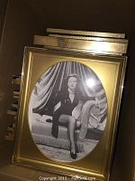 Stack of framed black and white photo prints and posters showing gold-tone frames and oval matting visible on the front piece.