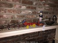 Full view of metal horse-drawn buggy with six horses and two figures, metal figurine of man in top hat, horse shoes and antique knife sharpener on fireplace mantle against a brick wall.