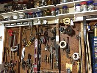 Pegboard and shelf display showing jars containing nails and screws above pegboard with hanging hand tools including levels, hand saw cores, screwdrivers, clamps, and hand drills.