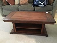 Front view of wooden coffee table with plank top and lower shelf, positioned in front of a green couch.