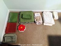 Overview of the collection showing green and red placemats, crocheted hotplates, and white and cream linens folded and laid on the floor.