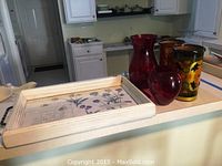 View of wooden serving tray and collection of glass and wooden vases on countertop