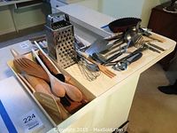 Wide shot showing an assortment of wooden and metal kitchen utensils spread out on a counter, including spoons, spatula, grater, and measuring cups.