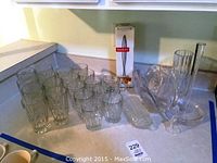 Photo showing 16 glass cups, some faceted and some smooth, arranged on a counter with a Bodum box in the background