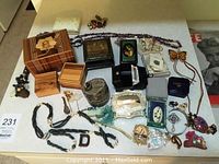 Overview of all costume jewelry and boxes laid out on table; includes amethyst chip necklaces, carved pins, wooden and silver-tone boxes.