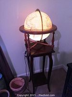 Light up globe on wooden stand, large circular globe with vintage map illuminated, placed on a tall wooden stand with four legs and crossbars.