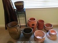 Overall view of various clay vases and planters arranged by window, includes dark brown pot, terracotta vase with holes, small pots, and marbled bowl