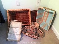 Photo showing three wicker baskets including rectangular and oval shapes, woven bowl and wooden bread tray leaning against a wall corner.