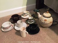 Full lot photo showing Grasslands Road tea pot and seven assorted tea cups with saucers arranged on carpet floor.