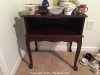Full view of cherry wood side desk table with various decorative items on top and some items on the floor around it.