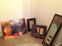 Four pieces of art grouped in corner showing overall lot including Warren Kimble signed vertical tree and house print, two smaller framed prints, and larger floral wood piece.
