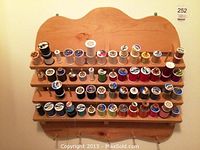 Front view of the wooden spool display rack holding various thread spools arranged neatly on four rows of prongs.