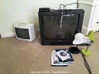 Magnavox black CRT TV, Sharp white CRT TV, two desk lamps, and weight loss books/DVDs on carpeted floor