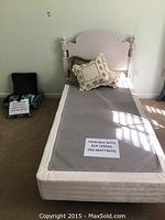 Photo showing the full twin bed with white wooden headboard, box spring, and bedspread including pillows on top.