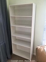 Front view of the white wooden bookshelf showing five shelves and adjustable peg holes along the sides.