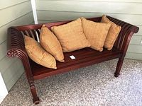 Full view of bench on porch showing slatted seat and back, curved arms, and all five pillows arranged across seat.
