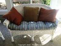 Front view of white wicker settee with three accent pillows and striped seat cushion.