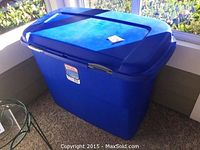 Closed large blue Sterilite plastic storage bin with lid, taken indoors near a window.
