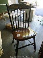 Wooden chair with dark frame and lighter wood seat seen from an angle, showing carved pineapple decoration on backrest and some scratches on the seat.